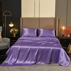 a bed with purple sheets and pillows in a room next to a couch, chair and lamp