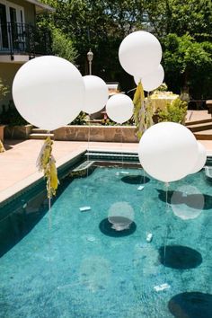 some balloons floating in the air near a swimming pool with clear blue water and greenery