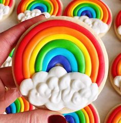 a rainbow cookie is being held by someone's hand with cookies in the background