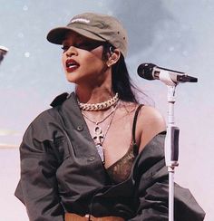 a woman wearing a hat and holding a guitar while standing in front of a microphone