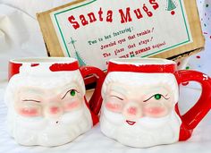 two santa mugs sitting next to each other on a white surface with a sign in the background