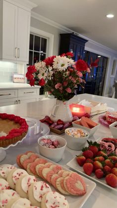 a table filled with desserts and pastries on top of white counter tops next to a vase full of flowers