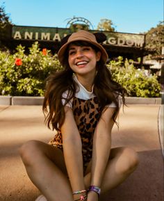 a young woman sitting on the ground wearing a hat and smiling at the camera with her legs crossed