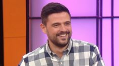 a man with a goatee smiles while sitting in front of a purple and orange wall