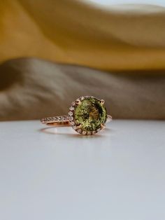 an oval cut green tourmaline and diamond ring on a white surface with a yellow cloth in the background