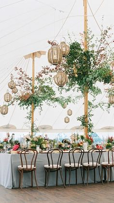 an outdoor tent with tables and chairs set up for a wedding reception under hanging lanterns