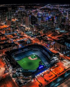 an aerial view of a baseball stadium in the city at night with lights on it