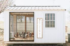 a small white building with a caged in area on the outside and doors open