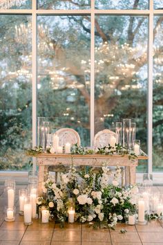 a table with candles and flowers on it in front of a large window filled with windows