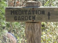 a wooden sign that says meditation garden on it's side in front of some trees