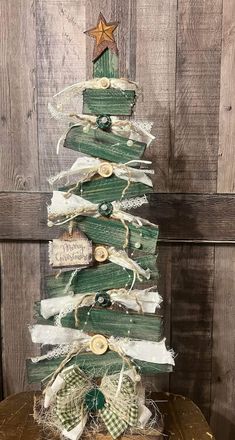 a small christmas tree made out of wood and ribbons with buttons on the top, sitting on a wooden table