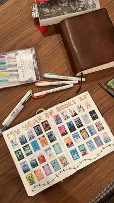 an open book sitting on top of a wooden table next to some pens and pencils