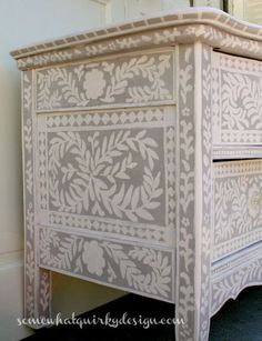 an old dresser painted white and decorated with intricate designs on the top, along with a mirror above it