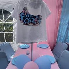 a t - shirt is displayed on a table in front of a pink and blue tent