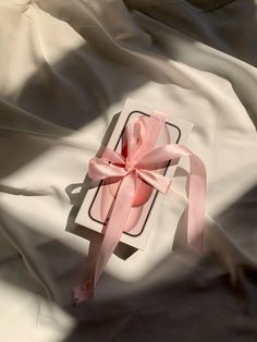 an open gift box with a pink bow on it sitting on top of a white sheet