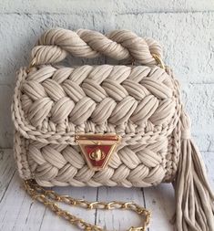 a white purse with a gold handle and tassell on the front, sitting on a wooden floor