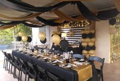 a table set up for a party with black, gold and white balloons hanging from the ceiling