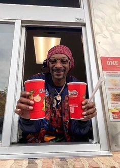 a man holding two red cups in front of a window