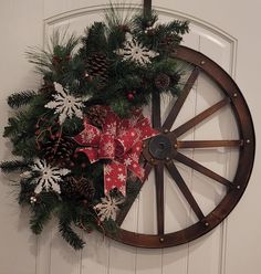 a christmas wreath with pine cones and bows on a wagon wheel hanging from the wall