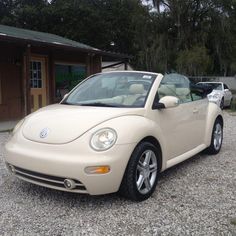 a beige convertible car parked in front of a building with trees and gravel around it