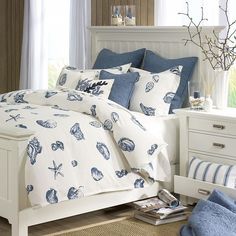 a white bed with blue and white sea shells on it, along with two nightstands