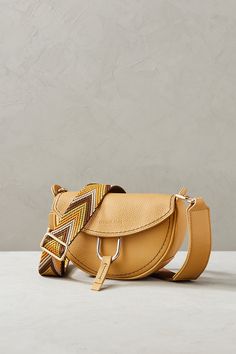 Brighten up your everyday look with the sunny Sol, a petite crescent-shaped shoulder bag with uniquely stylish accents. Beautifully crafted from rich, full-grain Italian calfskin with a pebbled texture, this handbag features an adjustable, removable shoulder strap with chevron ribbon detailing. The top flap, secured by a magnetic snap closure, is adorned with a subtly stamped Overland logo and a U-shaped metal clip with leather pull-tab for easy opening. Inside, you'll find space for small essen Modern Textured Leather Saddle Bag, Modern Textured Leather Crossbody Saddle Bag, Trendy Leather Saddle Bag For Work, Business Briefcase, Crescent Shape, Leather Pulls, Italian Leather, Everyday Look, Leather Backpack