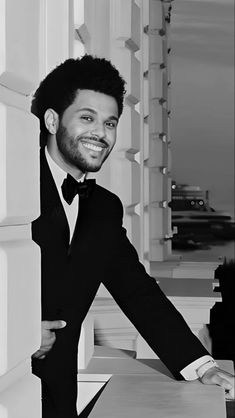 a black and white photo of a man in a tuxedo leaning against a wall