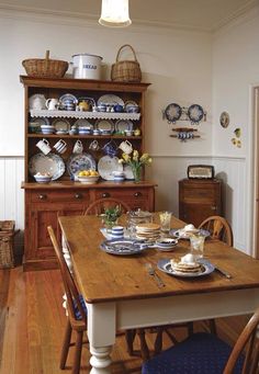 a wooden table topped with plates and bowls next to a hutch filled with dishes