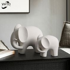 two white elephants are standing on top of a black table next to an open book