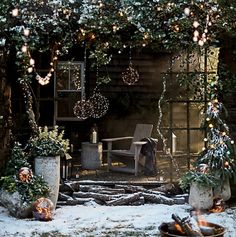 an outdoor fireplace surrounded by potted plants and trees with lights on them in the snow