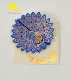 a blue and gold peacock brooch sitting on top of a piece of white paper