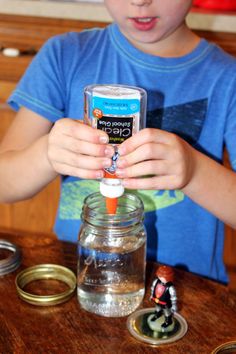 a young boy holding an orange object in front of a jar on top of a table