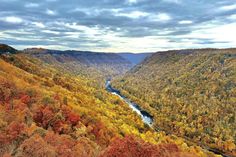 a river flowing through a valley surrounded by autumn colored trees in the mountains and hills