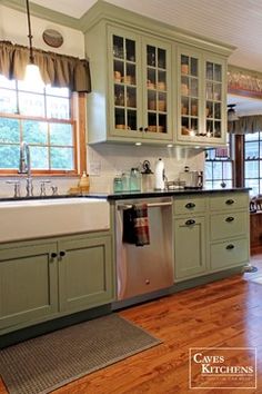 a kitchen with wooden floors and green cabinets in the center, along with a white sink and dishwasher