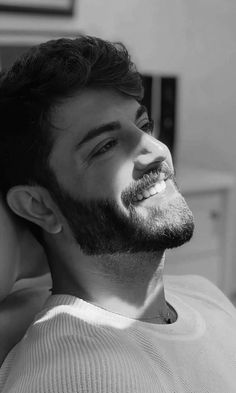 a black and white photo of a man with a beard smiling at something in the distance