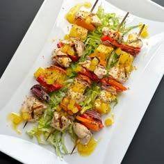 a white plate topped with chicken and veggies on skewered skewers