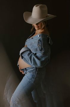 a pregnant woman in jeans and a cowboy hat poses for the camera with her stomach exposed