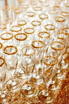 champagne glasses lined up on a table with gold sequins and glitter around them