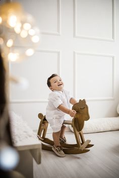 a little boy that is sitting on a wooden rocking horse in a room with white walls