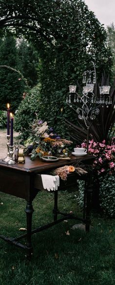 a table with candles and flowers on it in the middle of some grass next to bushes