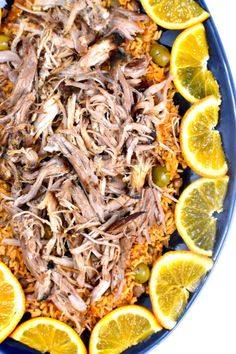 a blue plate topped with meat and rice covered in orange slices next to sliced lemons