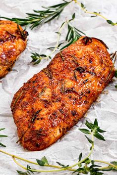 two pieces of grilled chicken sitting on top of a piece of wax paper with green sprigs