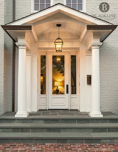 the front entrance to a house with white pillars and lights on it's sides