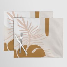 two place mats with silverware on them, one has a palm leaf design and the other has a gold colored fork