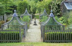 an iron gate with statues on it in the middle of a garden filled with flowers