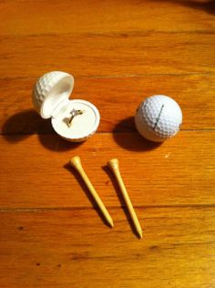 two golf balls and tees on a wooden floor with one missing the hole in the middle