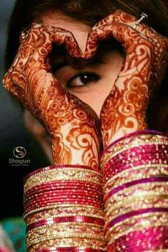 a woman's hands with hennap and bracelets on her face, making the shape of a heart