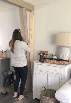 a woman standing next to a white dresser in a living room with a wooden cross on the wall