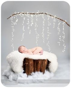 a baby is laying on top of a tree stump with white beads hanging from it