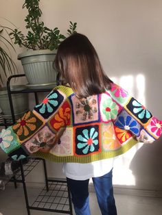 a woman standing in front of a potted plant wearing a multicolored sweater